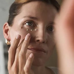 Close up of woman's mirror reflection applying Cellular Performance Extra Intensive Eye Cream with their fingers